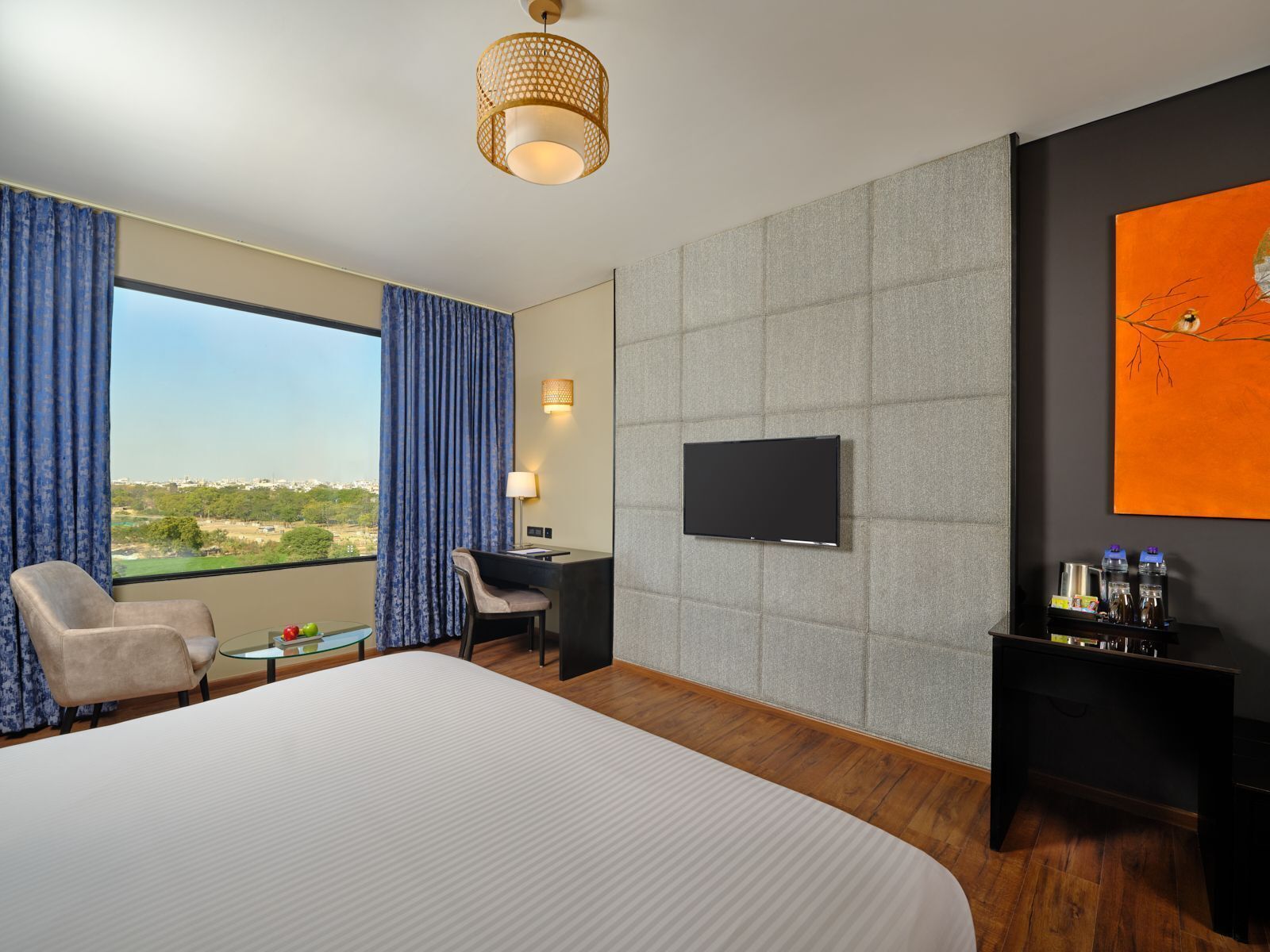 A hotel room with a large bed, a desk, a chair, a TV, and a view of the city.