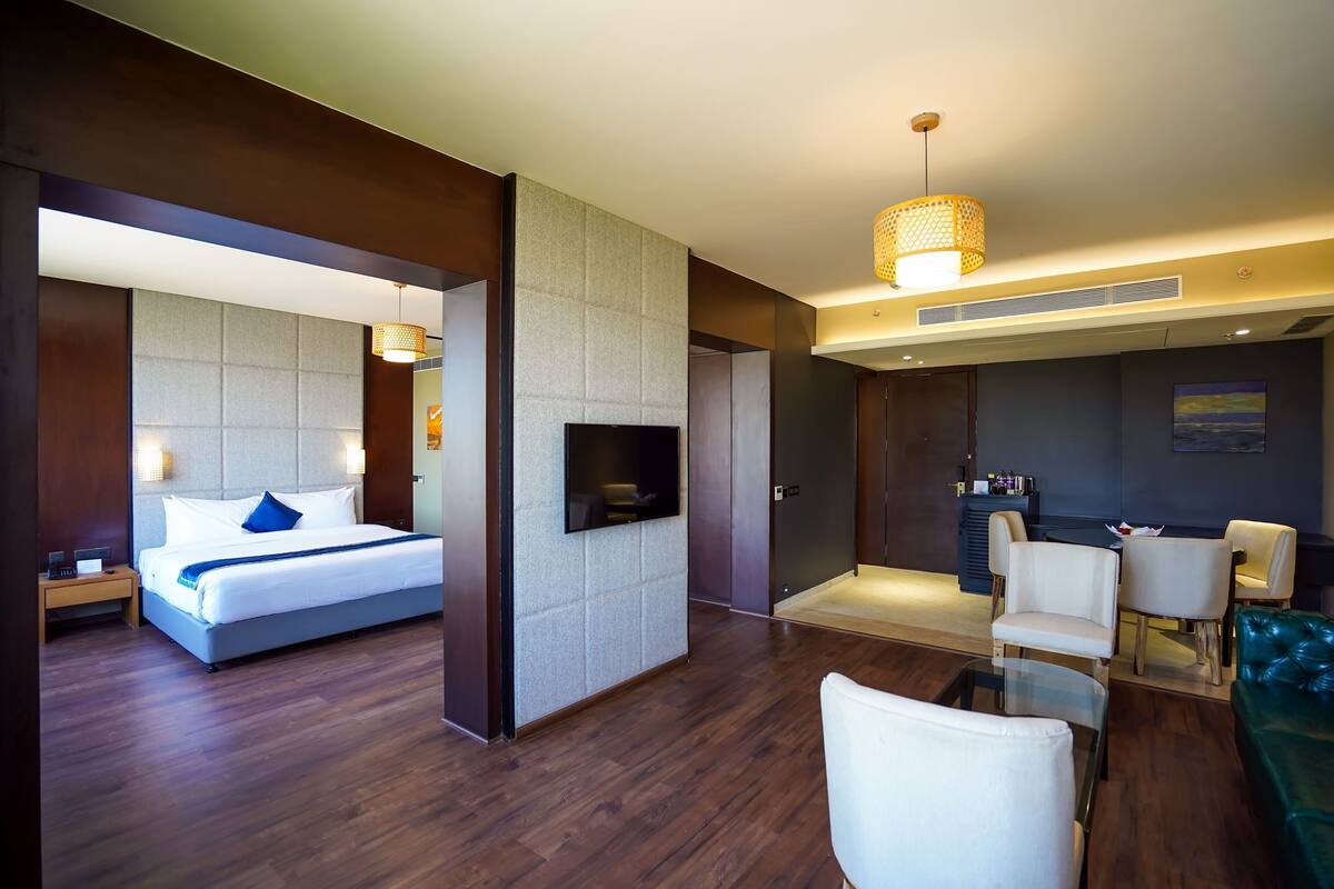 A modern hotel room with a bed, a TV, a seating area with chairs, and a sofa.