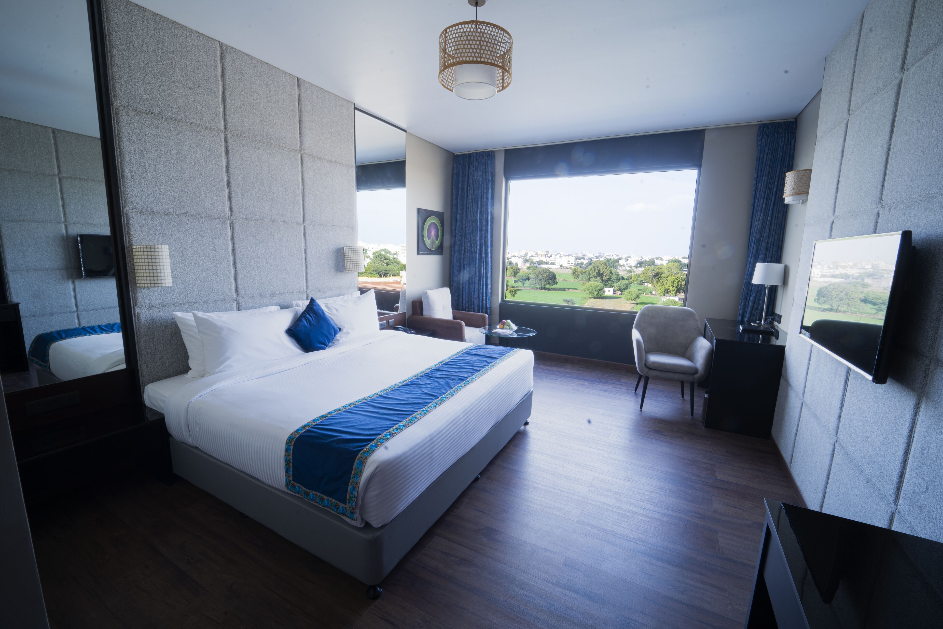 A modern hotel room with a large bed, a desk, a chair, and a TV.