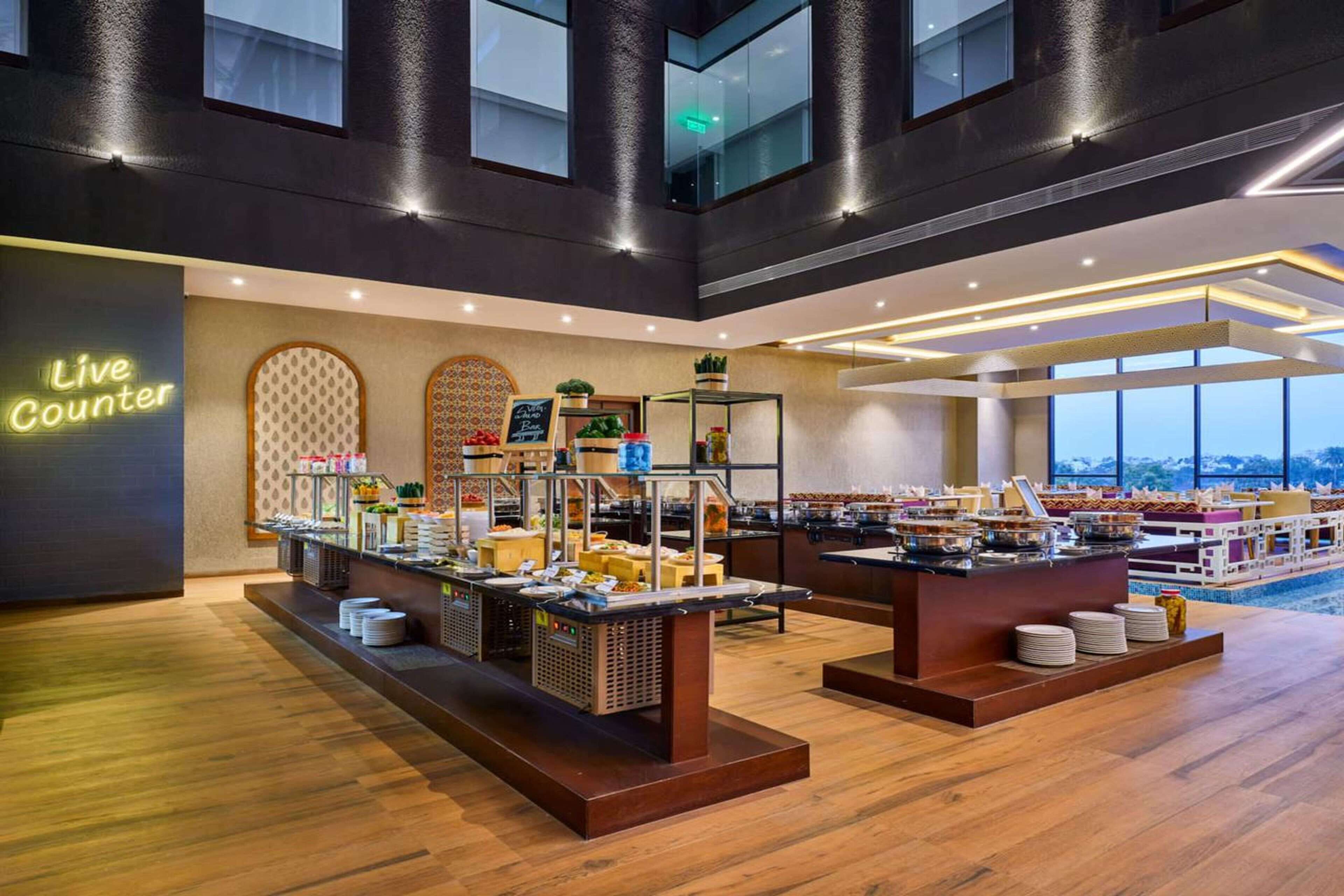 A hotel lobby with a 'Live Counter' sign, buffet setup, and large windows offering a view.