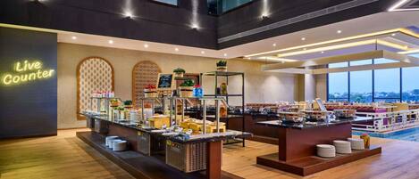 A hotel lobby with a 'Live Counter' sign, buffet setup, and large windows offering a view.
