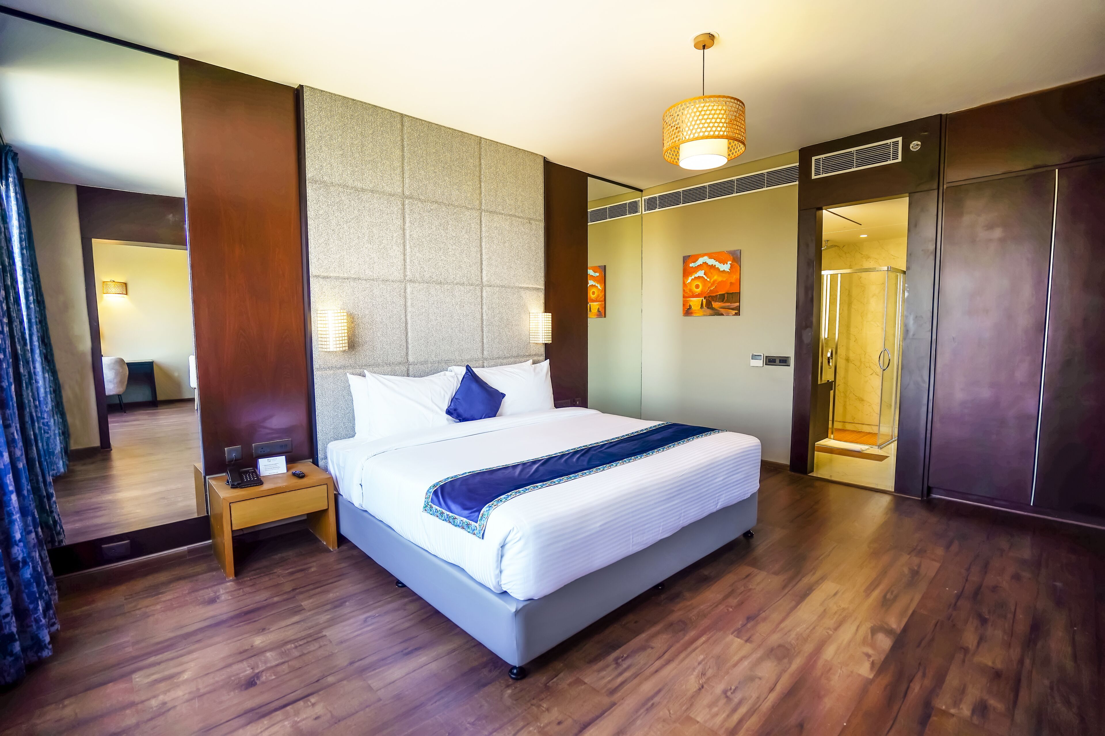 A hotel room with a large bed, a nightstand with a phone and a notepad, a mirror, a wooden floor, and a wardrobe.
