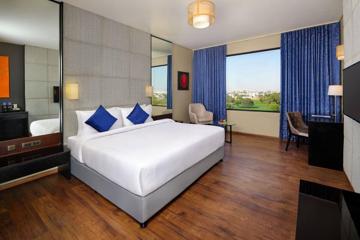 A hotel room with a large bed, a desk, a chair, a TV, and a view of the city.