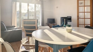 A sunlit room with a round table, chairs, a television, and a door with glass panels.