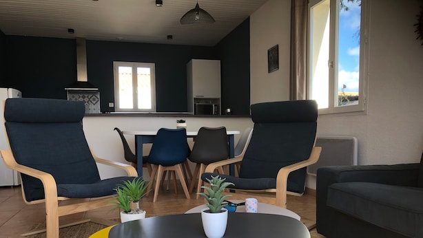 A modern living room with two armchairs, a sofa, a small table, and a dining area with chairs and a table.
