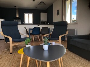 Ein modernes Wohnzimmer mit zwei Sesseln, einem Sofa, einem kleinen Tisch und einem Essbereich mit Stühlen und einem Tisch.