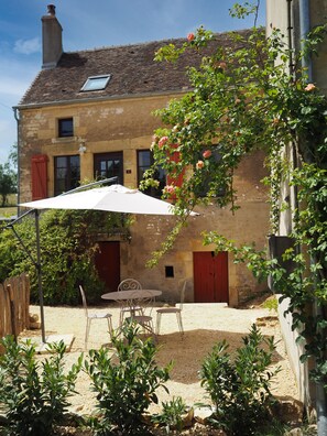 Ein rustikales Steinhaus mit Ziegeldach, einem Balkon mit weißem Sonnenschirm und einem Gartenbereich mit Tisch und Stühlen.