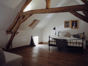 Ein Schlafzimmer mit schrägverdeckter Decke, Holzbalken, einem Bett mit floralem Bettbezug und zwei gerahmten Bildern an der Wand.