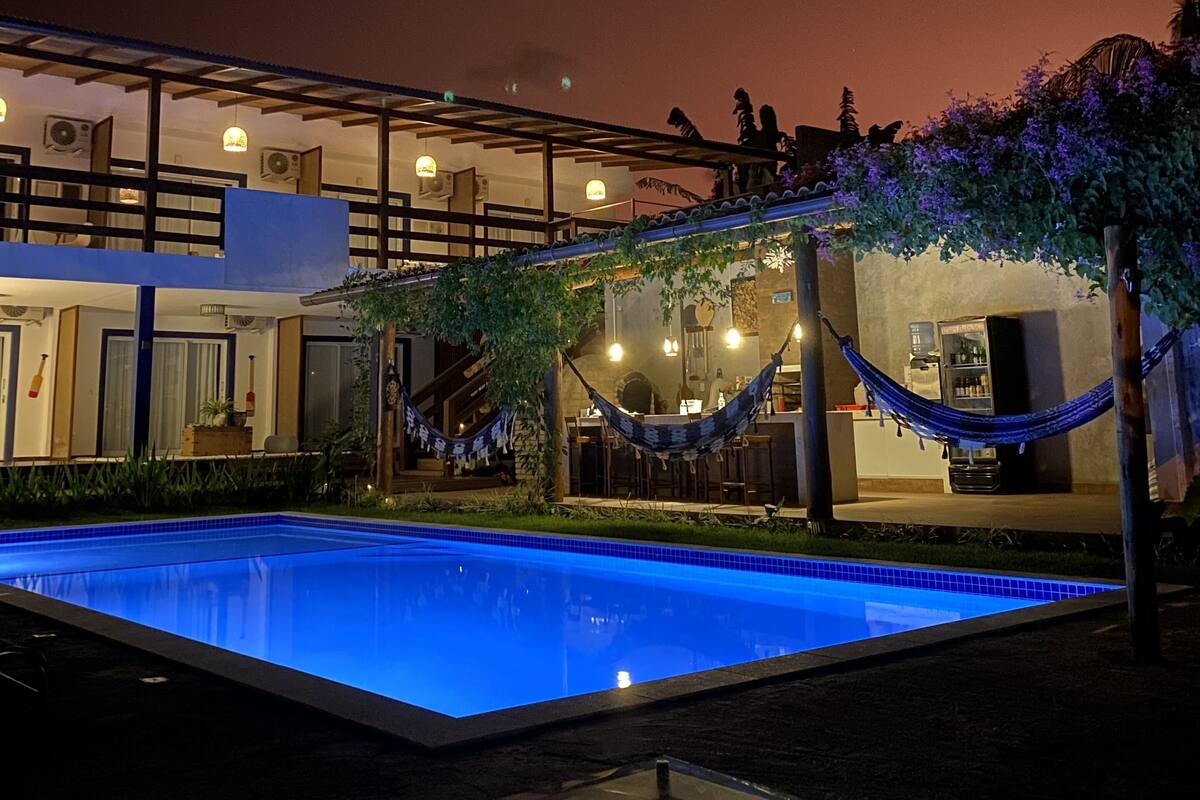 Un área de piscina nocturna con una hamaca, un elemento acuático y una zona de bar.