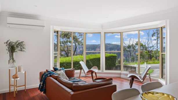 A modern living room with a large window offering a scenic view, a brown leather sofa, and a dining area with a white table and chairs. - outstanding escarpment and valley views, close to lookouts and bushwalks (Katoomba)