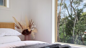 A bedroom with a large window, a bed with white pillows, a book titled "CHANEL," and a vase with dried flowers. - outstanding escarpment and valley views, close to lookouts and bushwalks (Katoomba)
