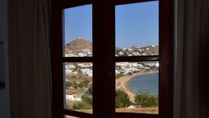A room with a large window overlooking a beach and a hill. - Petra Holiday Village (Ios)