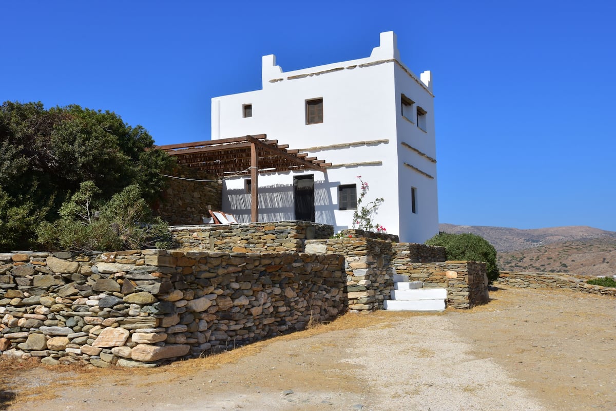 A white building with a stone wall and a wooden pergola.