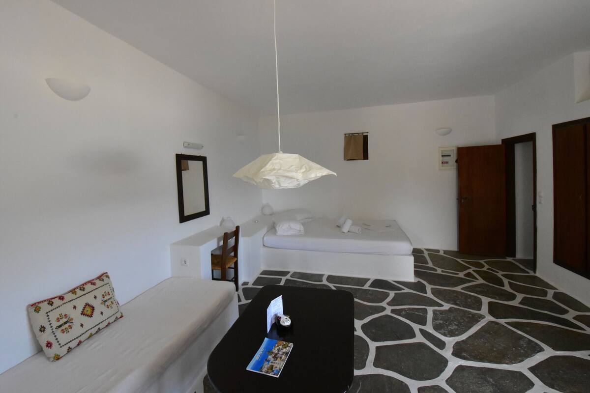A room with a stone floor, a white sofa, a black table with a brochure, a hanging light fixture, and a wooden door.