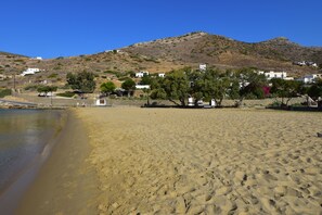 A sandy beach with white buildings and a hill in the background. - Petra Holiday Village (Ios)