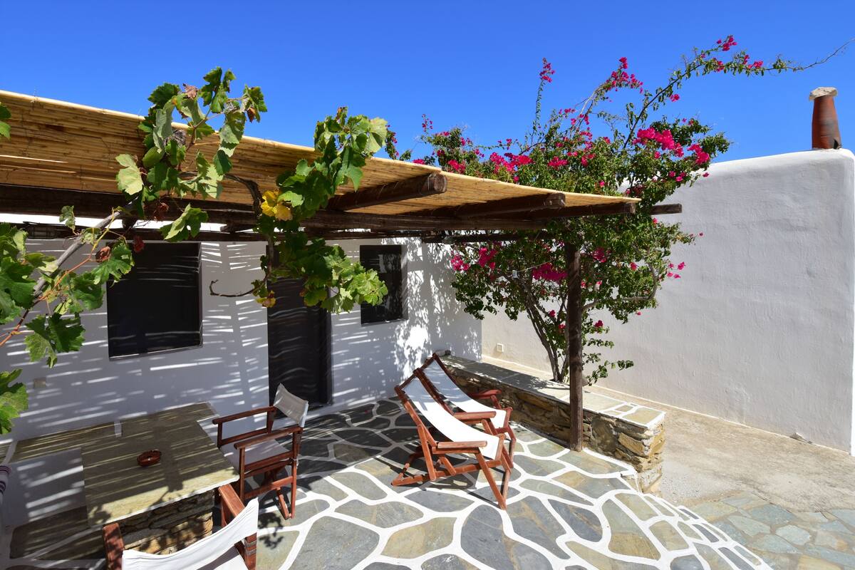 A patio with stone flooring, wooden furniture, and a pergola with climbing plants.