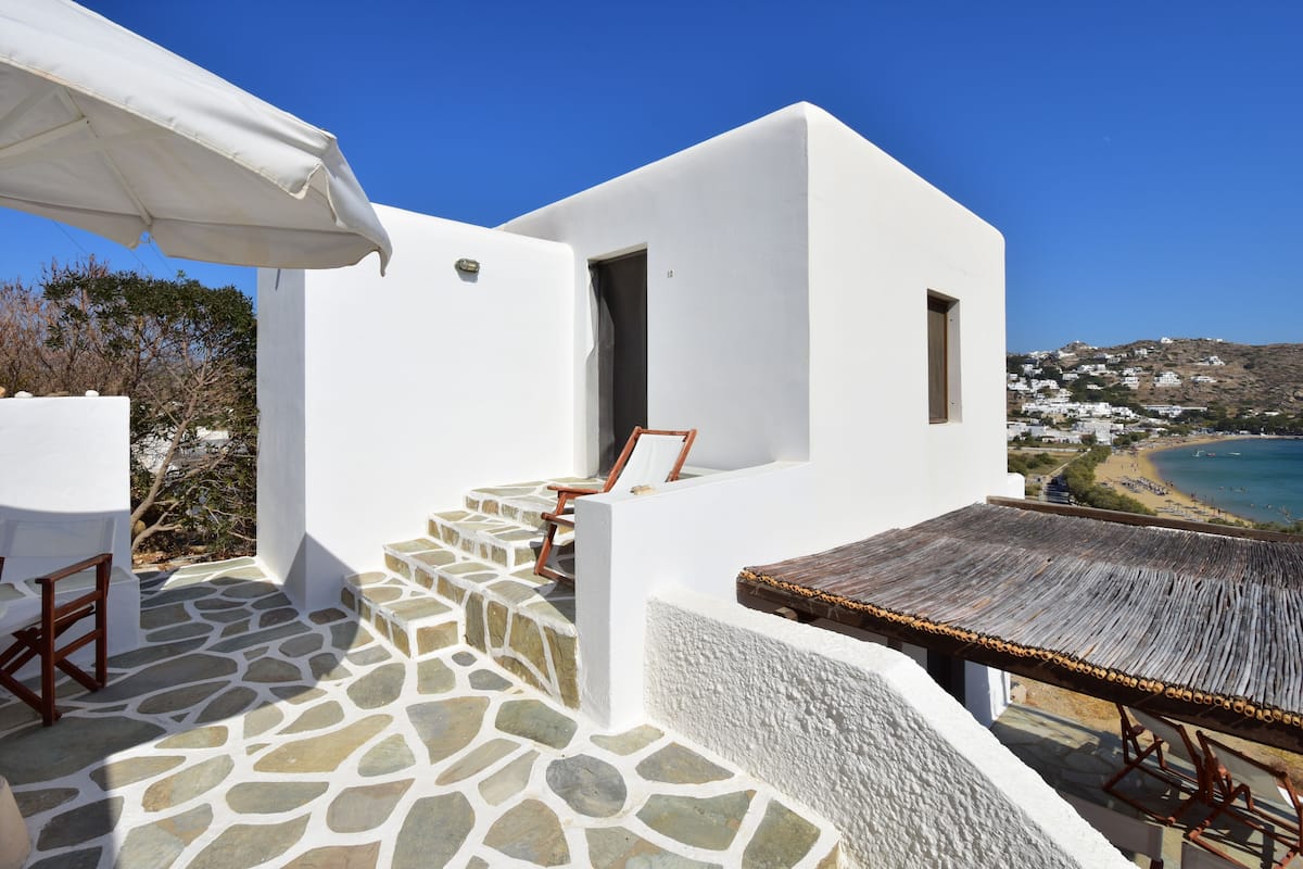 A white building with a stone floor, a wooden table, and a view of a beach.
