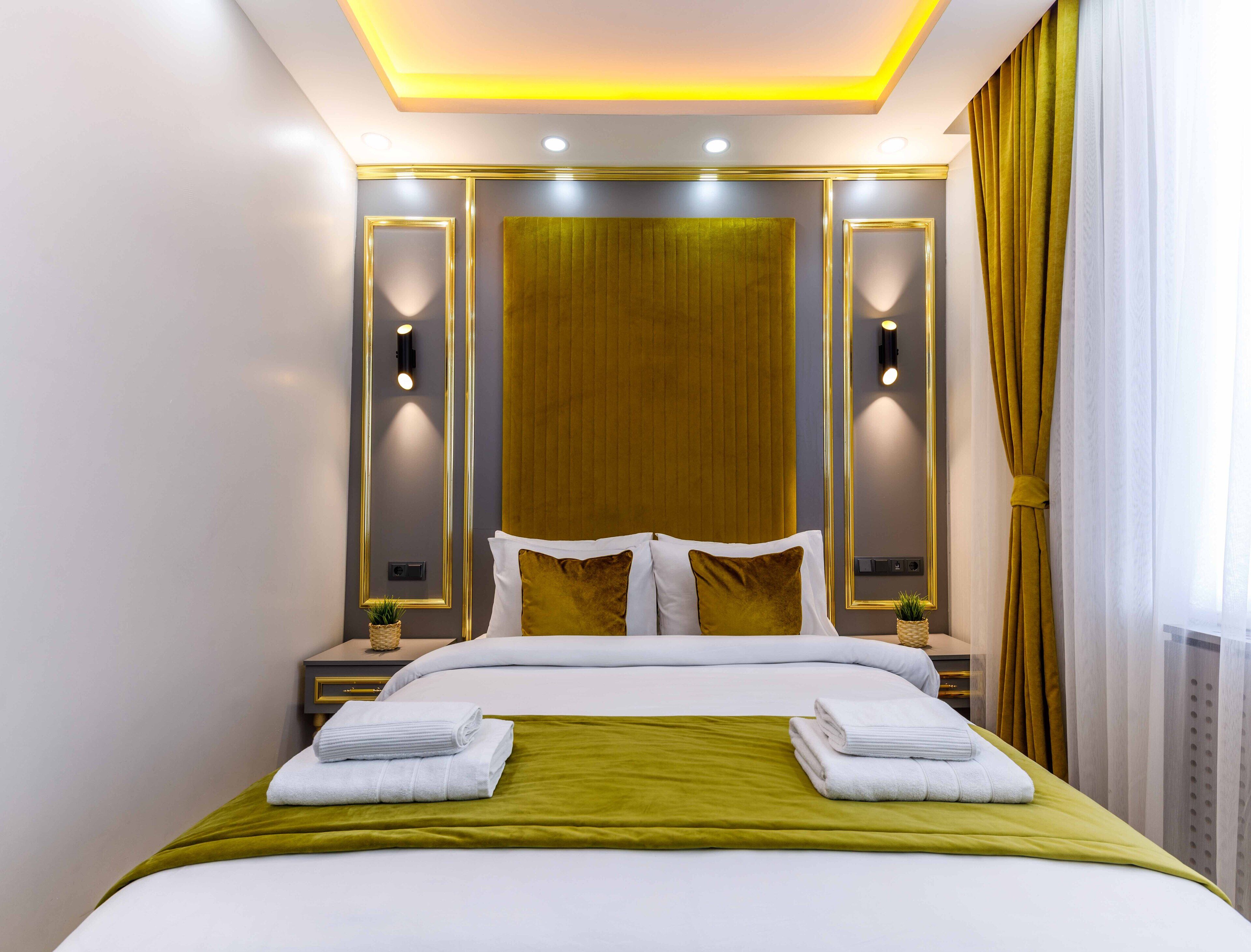 A modern hotel room with a large bed, two bedside tables, a headboard with integrated lighting, and a view of the outdoors through sheer curtains.
