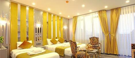 Habitación de hotel con dos camas, una zona de estar con una silla, una mesa y un espejo.