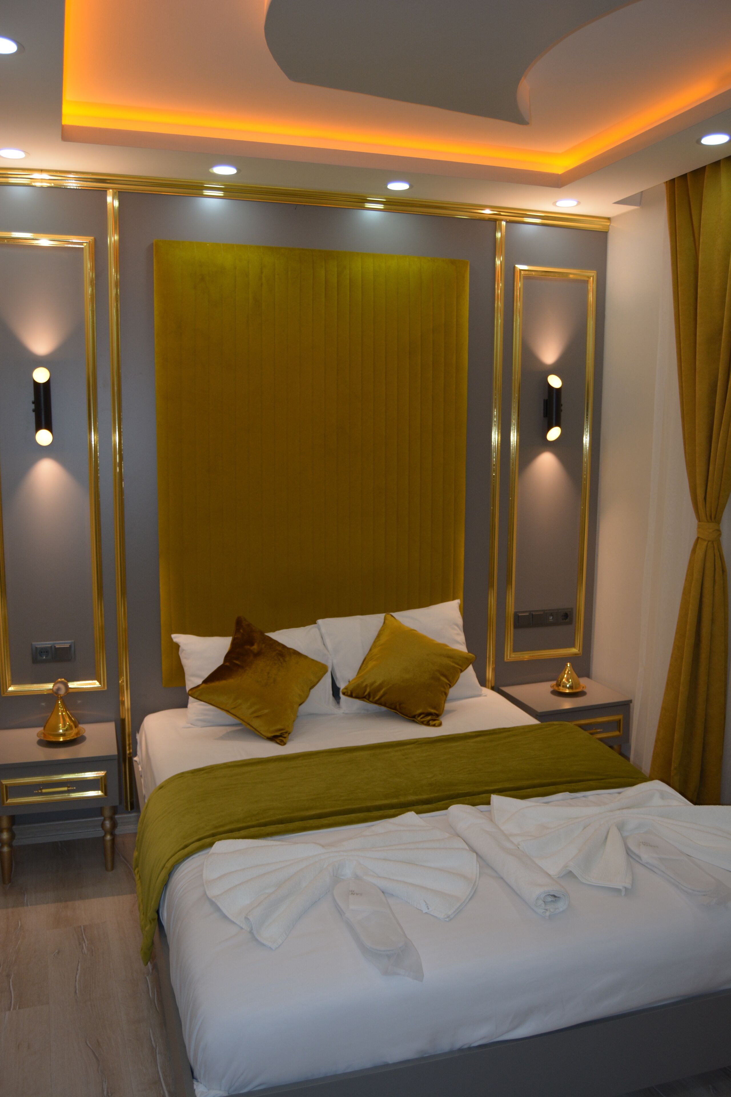 A modern hotel room with a large bed, gold accents, and a neutral color scheme.
