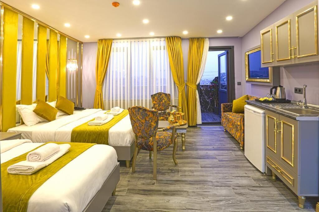 A hotel room with two beds, a dining area, a kitchenette, and a view through a door.