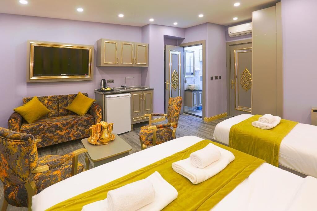 A hotel room with two beds, a sofa, a small kitchenette, and a TV.