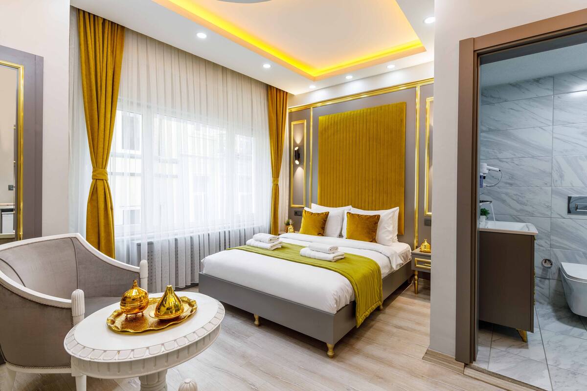 A modern hotel room with a bed, bedside tables, a chair, and a bathroom with a shower and toilet.