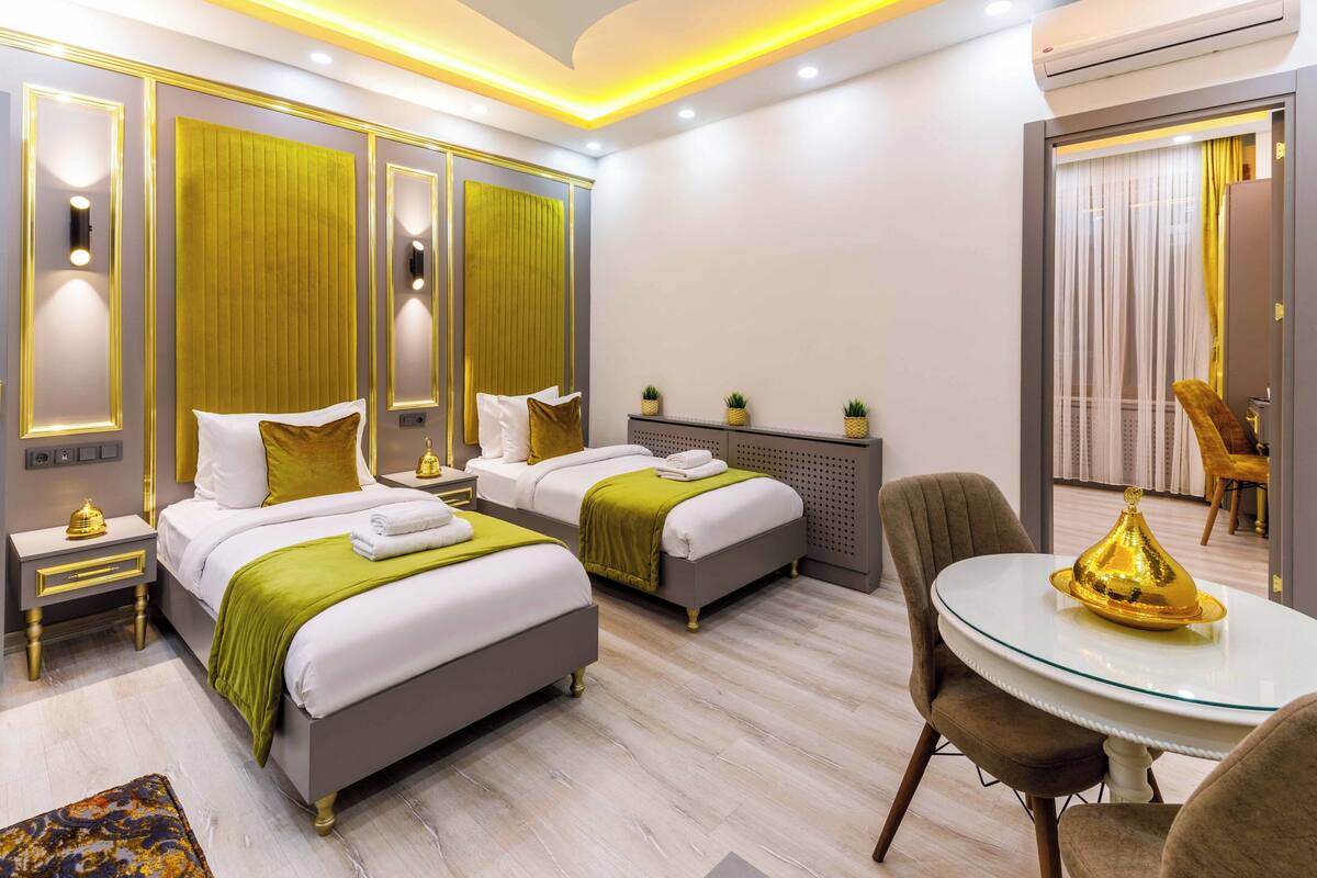 A modern hotel room with two beds, a dining table, and a seating area.