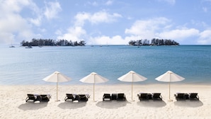 A beach with lounge chairs and umbrellas, a calm sea, and boats in the distance. - The Danna Beach Villas - A Member of Small Luxury Hotels of the World (Langkawi)