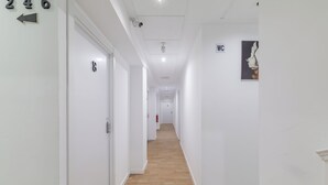 En gang med hvide vægge, nummererede døre og trægulv.