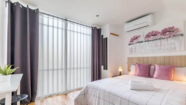 Et moderne hotelværelse med en stor seng, et skrivebord med stol, en potteplante og et billede på væggen.