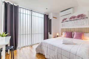 A modern hotel room with a large bed, a desk with a chair, a potted plant, and a painting on the wall. - LooP América - Adults Only (Madrid)
