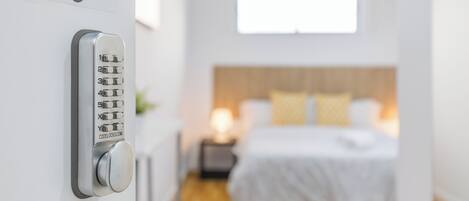 Una habitación de hotel moderna con una cama, una mesita de noche y un candado electrónico en la pared.
