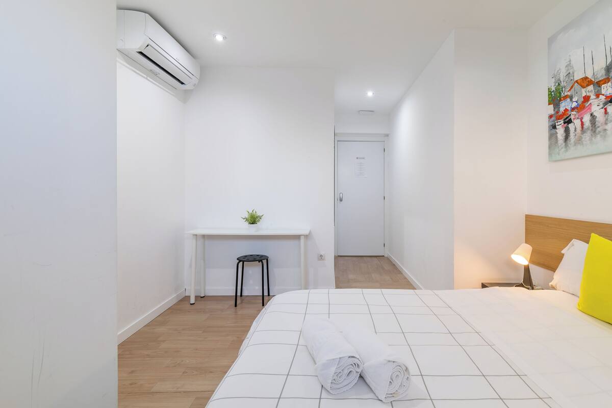 Una habitación de hotel con cama, escritorio, silla, mesita de noche y lámpara.