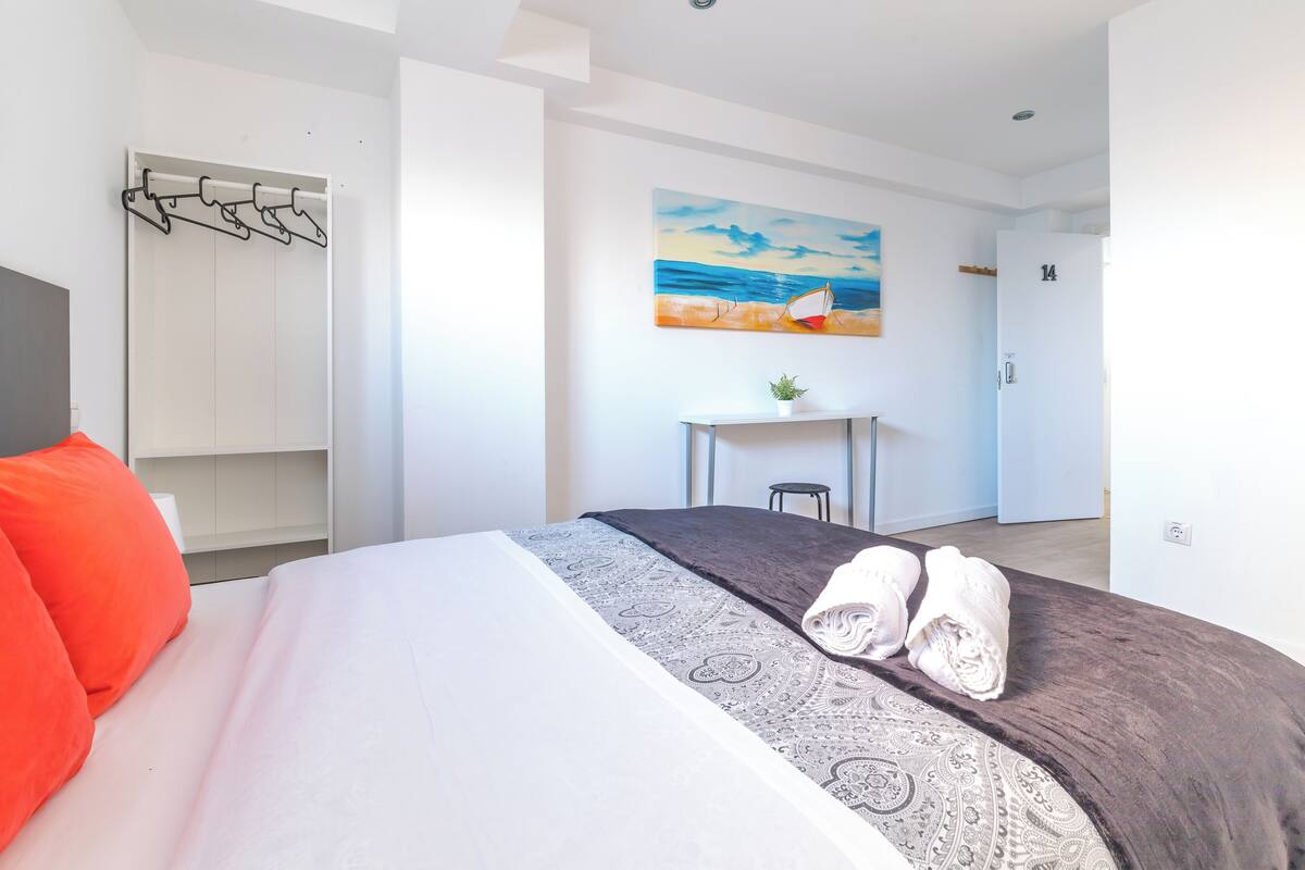 Una habitación de hotel con cama, escritorio, silla y un cuadro en la pared.