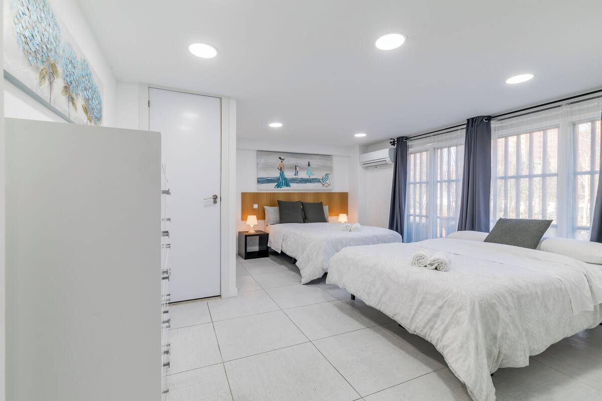 Una habitación de hotel con dos camas, cabecera de madera, una obra de arte en la pared y una ventana con cortinas.