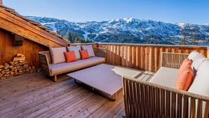 Un patio in legno con divano e poltrone, un tavolo e una pila di legna da ardere.