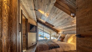 Una camera da letto con soffitto in legno, un letto con cuscini, un comodino e una finestra con persiane.