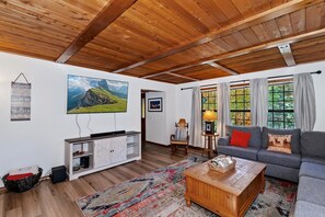A living room with a wooden ceiling, a sofa, a coffee table, a television, and a large window with curtains.