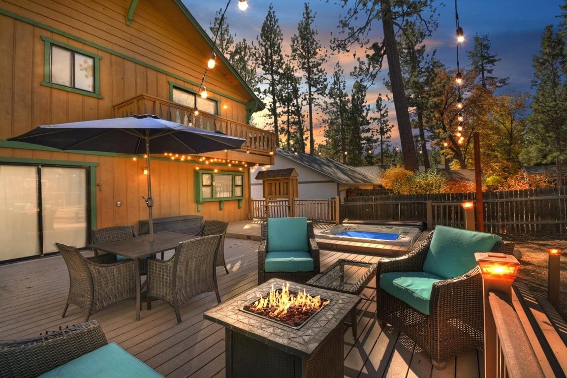 A wooden deck with outdoor furniture, a hot tub, and string lights.