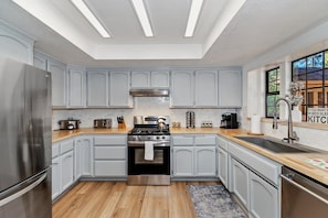 A modern kitchen with light grey cabinets, a stainless steel refrigerator, a gas stove, and a large window providing a view of the outdoors.