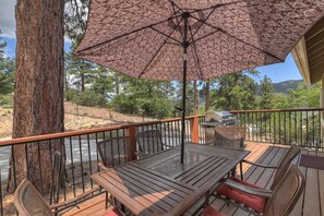 An outdoor patio with a table and chairs, a patterned umbrella, and a view of a river and trees.