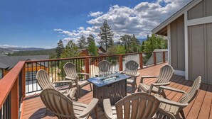 A deck with outdoor seating and a fire feature, overlooking a residential area with trees and mountains.