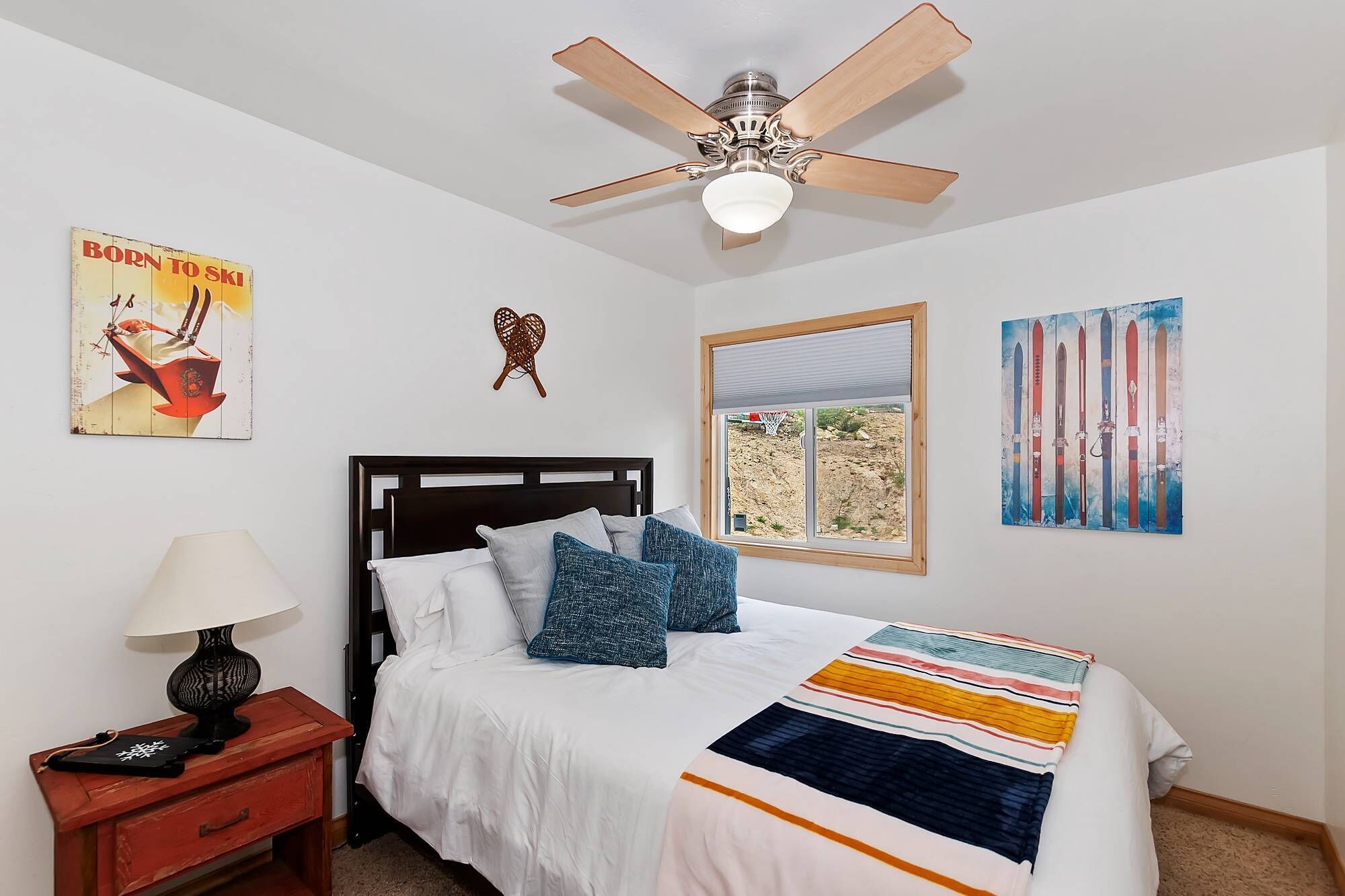 A bedroom with a bed, a nightstand, a ceiling fan, a window, and wall art.