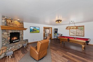 A room with a stone fireplace, a pool table, and a comfortable seating area.