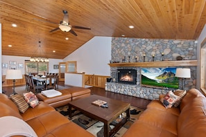 A spacious living room with a stone fireplace, leather sofas, and a dining area with a view.