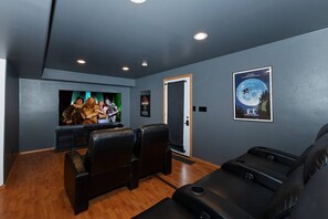 Sala de cine en casa con una televisión de pantalla plana grande, dos sillones de cuero negro y un cartel con una escena iluminada por la luna.