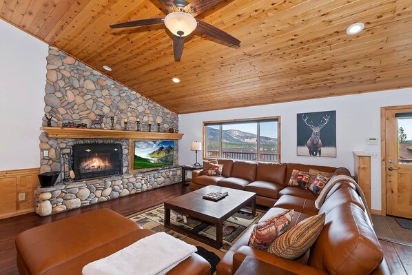 A cozy living room with a stone fireplace, leather furniture, and a ceiling fan.