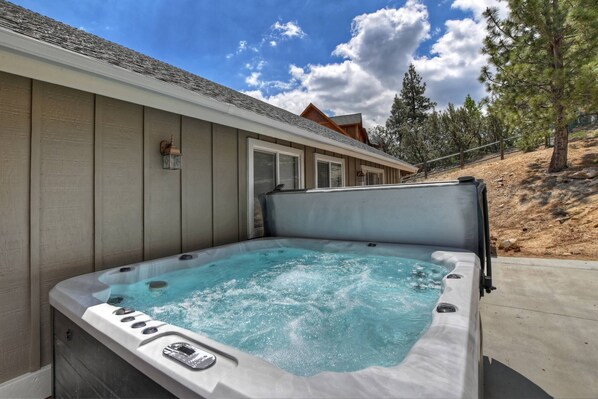 Un jacuzzi en un patio trasero con una terraza de madera y una casa al fondo.