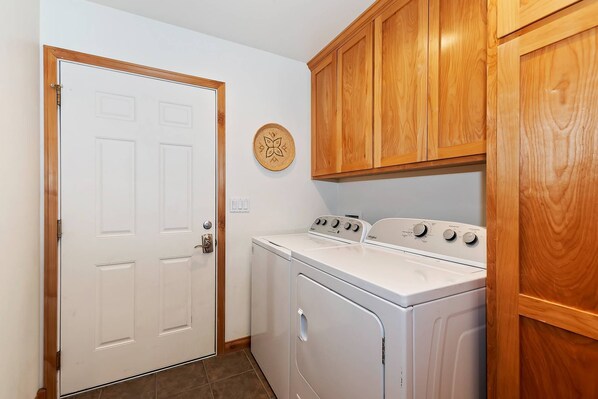 A laundry room with a white washer and dryer, wooden cabinets, and a door with a brass handle.